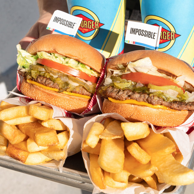 Picture of a tray of Impossible burger, fries, and drinks being held by someone