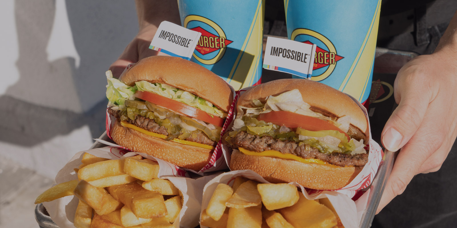 Picture of a tray of Impossible burger, fries, and drinks being held by someone